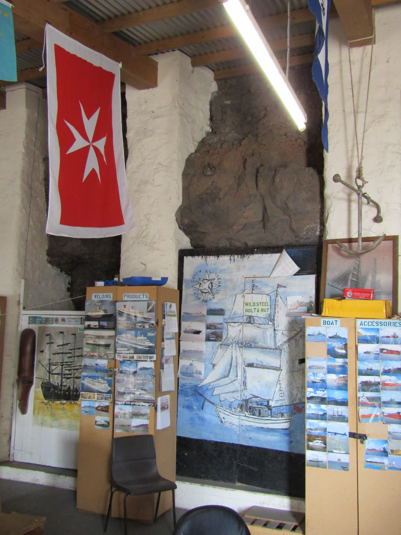 The inside of the fuel company office. It's interesting for two reasons: 1) It's built directly against the cliff face (note the white concrete pillars with the rock between them), and 2) The very large Maltese maritime insignia